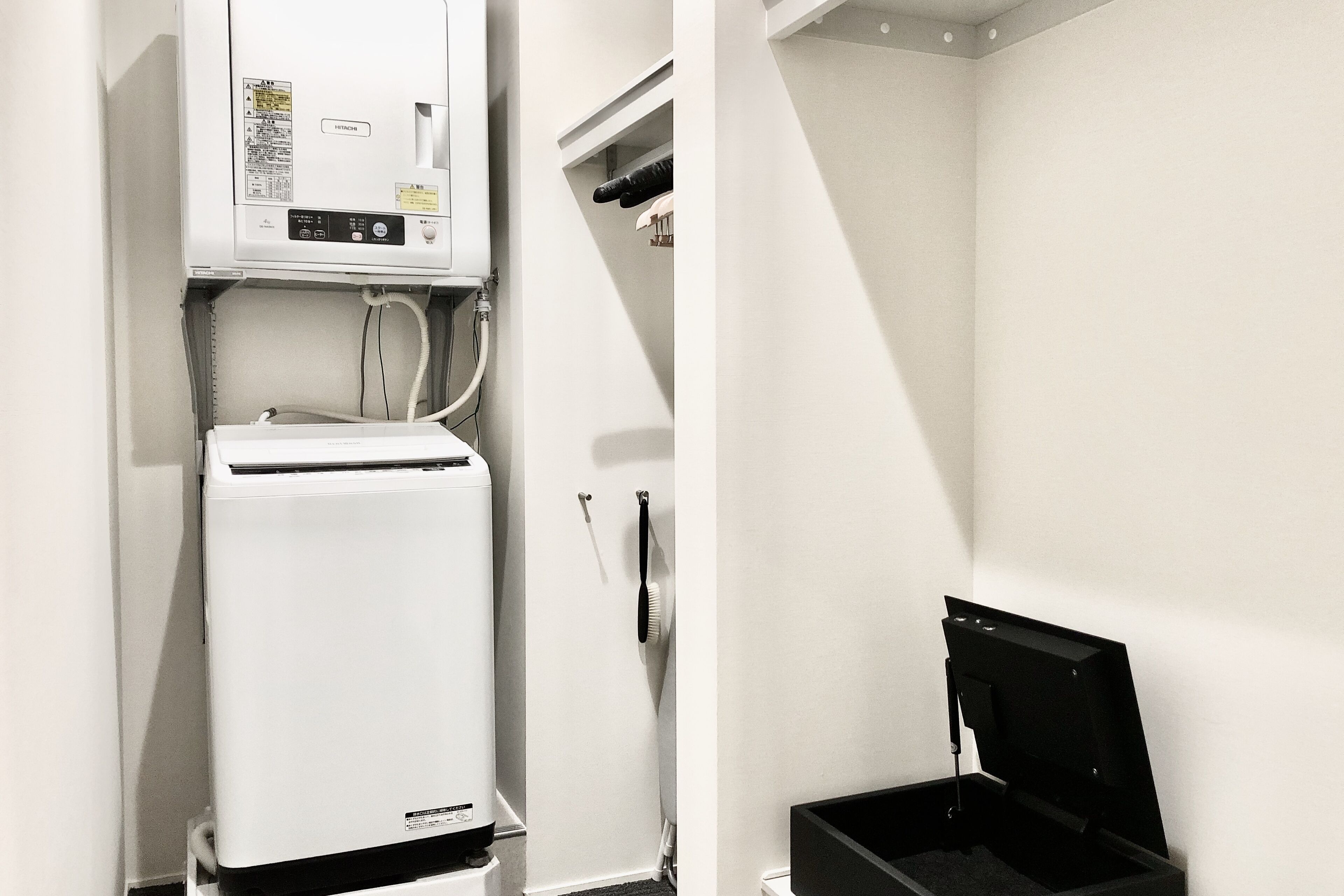 Een kleine kamer met een witte koelkast, een kleine zwarte prullenbak en een witte muur.