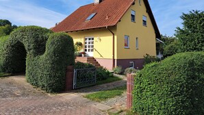 A yellow house with a red roof, a small porch, and a paved driveway. - Sylvana vacation apartment (Klein Vielen)