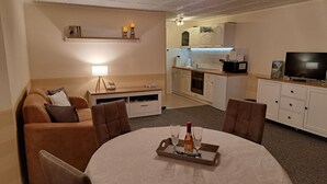 A cozy living area with a sofa, a dining table with a tray of drinks, a TV, and a kitchenette in the background. - Sylvana vacation apartment (Klein Vielen)