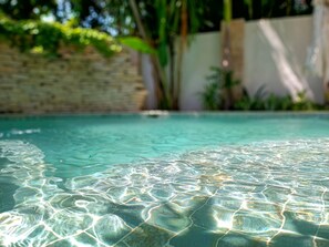 A clear pool with visible ripples and reflections, surrounded by greenery and a stone wall.