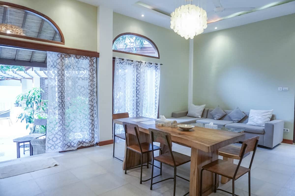 A dining area with a wooden table and chairs, a sofa, and a chandelier.
