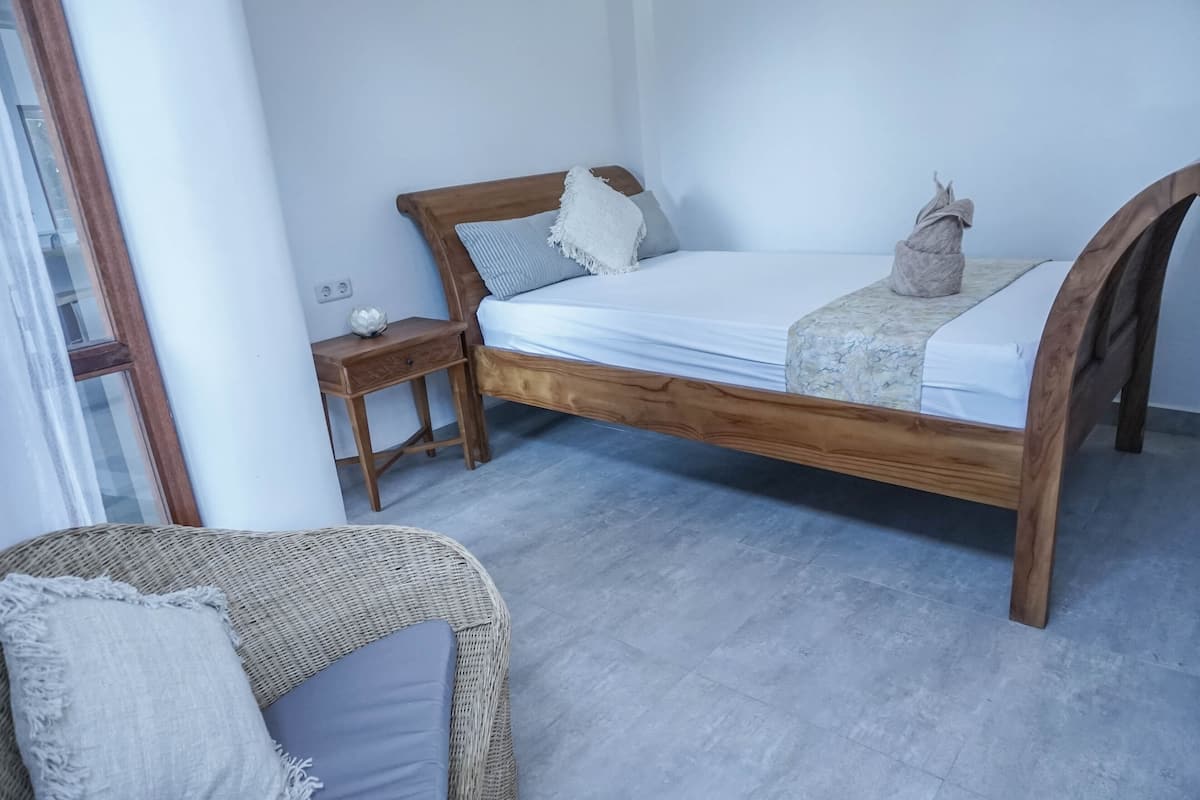 A bedroom with a wooden bed, a nightstand, a wicker chair, and a window.
