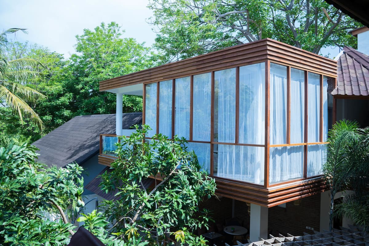 A modern house with a large glass window, surrounded by lush greenery.