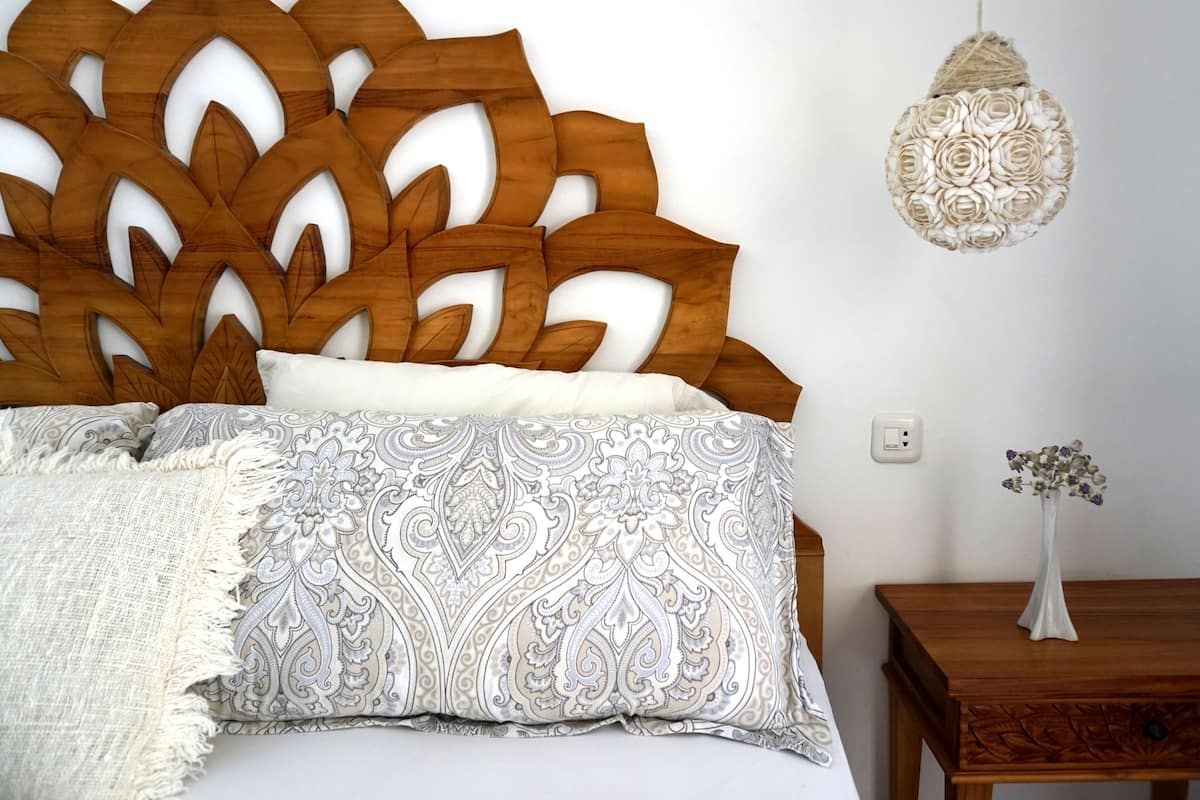 A bed with a wooden headboard, patterned pillows, and a white throw blanket.