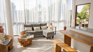 A bright, sunlit living room with a grey sofa, a glass coffee table, and a wooden bench. - Soraya Yoga Wellness Center (Gili Trawangan)