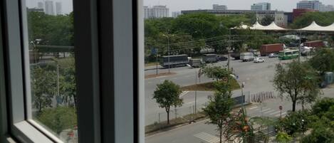 A view through a window of a cityscape with buildings, trees, and a road with vehicles.
