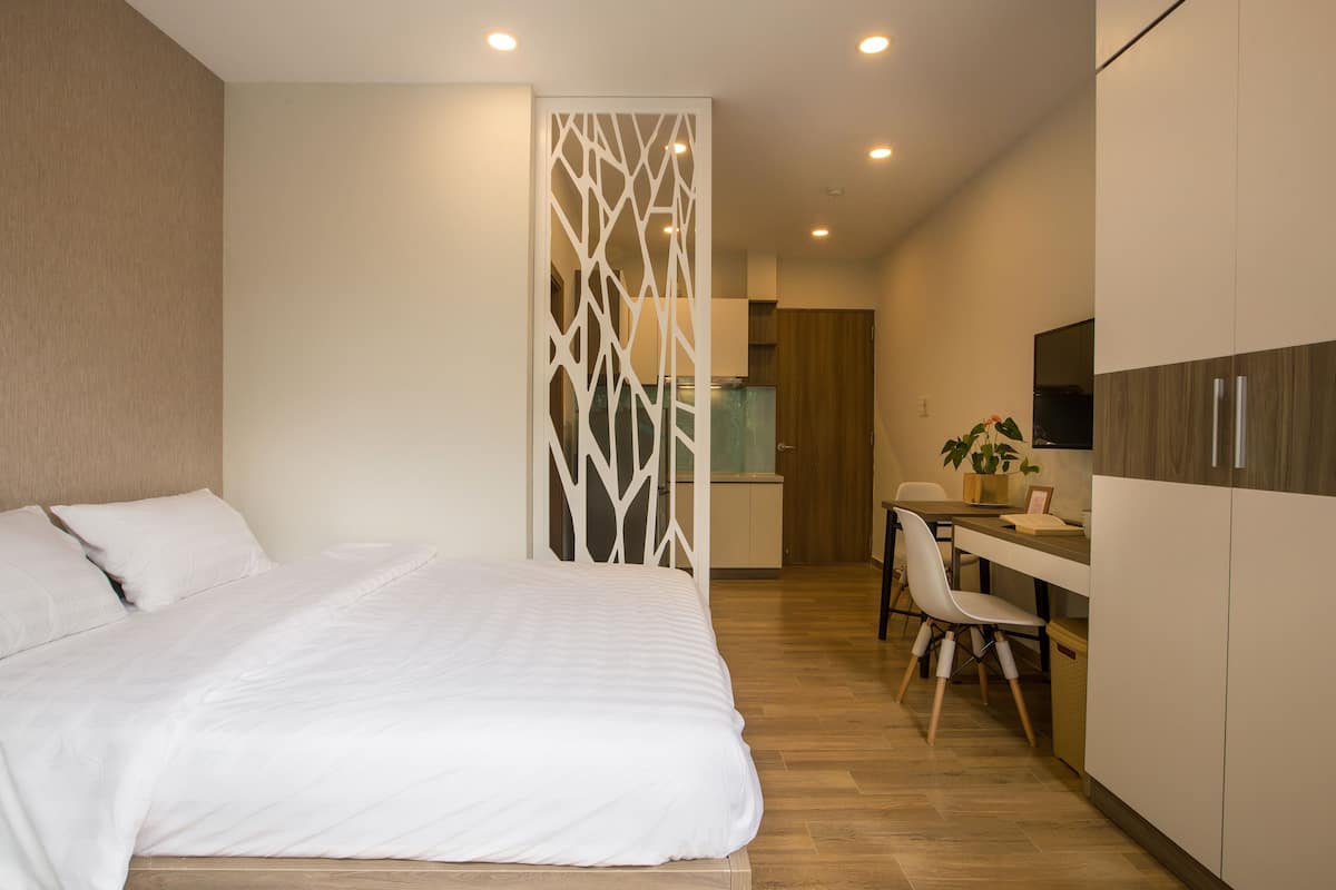Een moderne hotelkamer met een groot bed, een bureau met stoel, een kitchenette en een decoratieve scheidingswand.