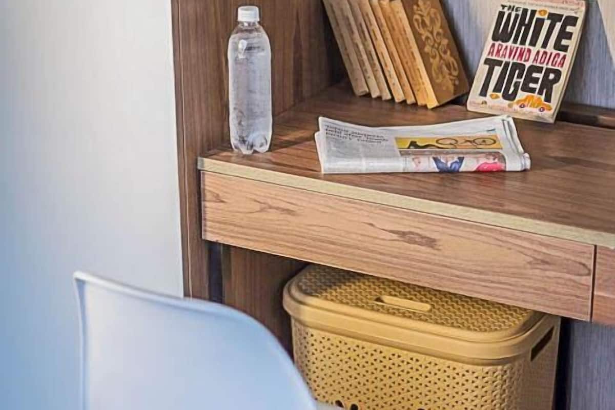 Een klein houten bureau met een waterfles, een tijdschrift en een bordje met de tekst 'WHITE ARAVIND ADIGA TICER'.