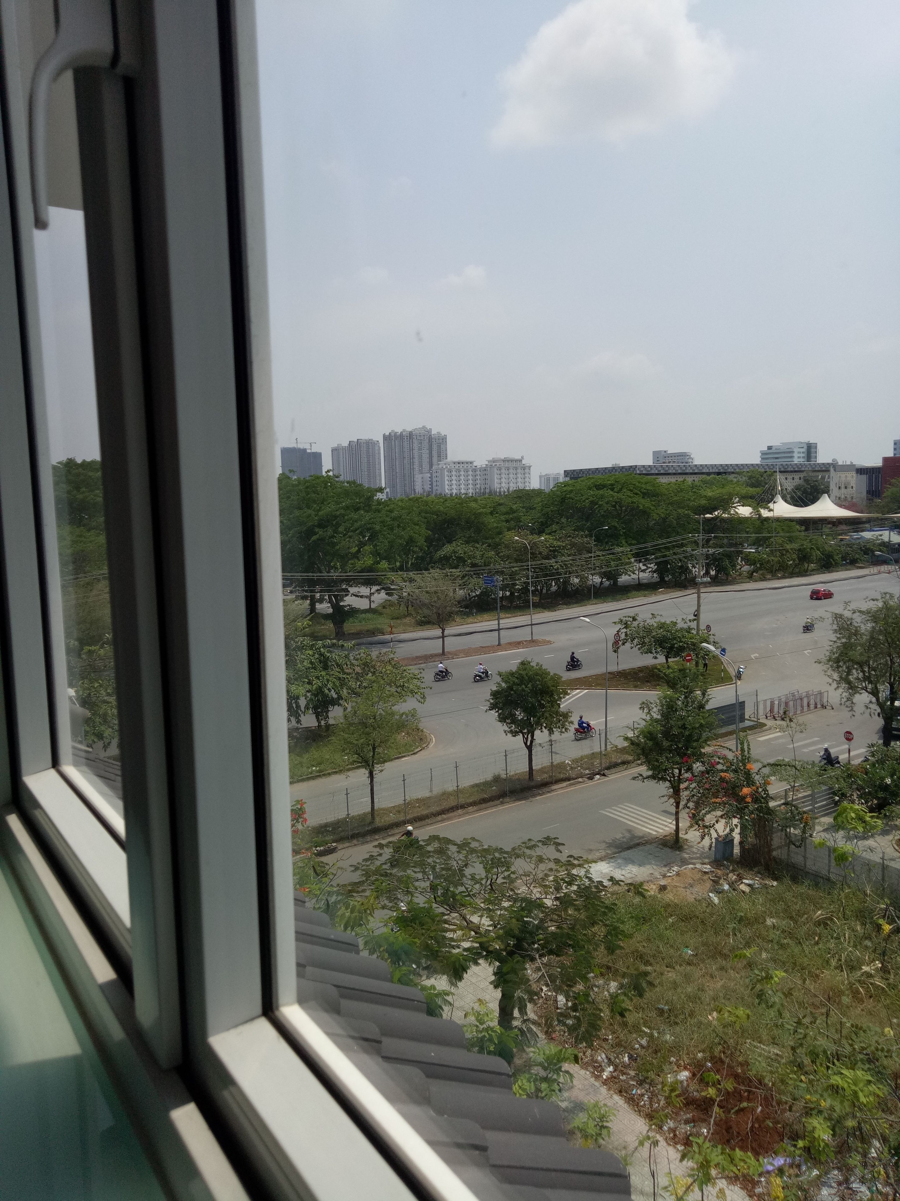 Blick aus einem Fenster auf eine Stadtstraße mit Gebäuden, Bäumen und blauem Himmel.
