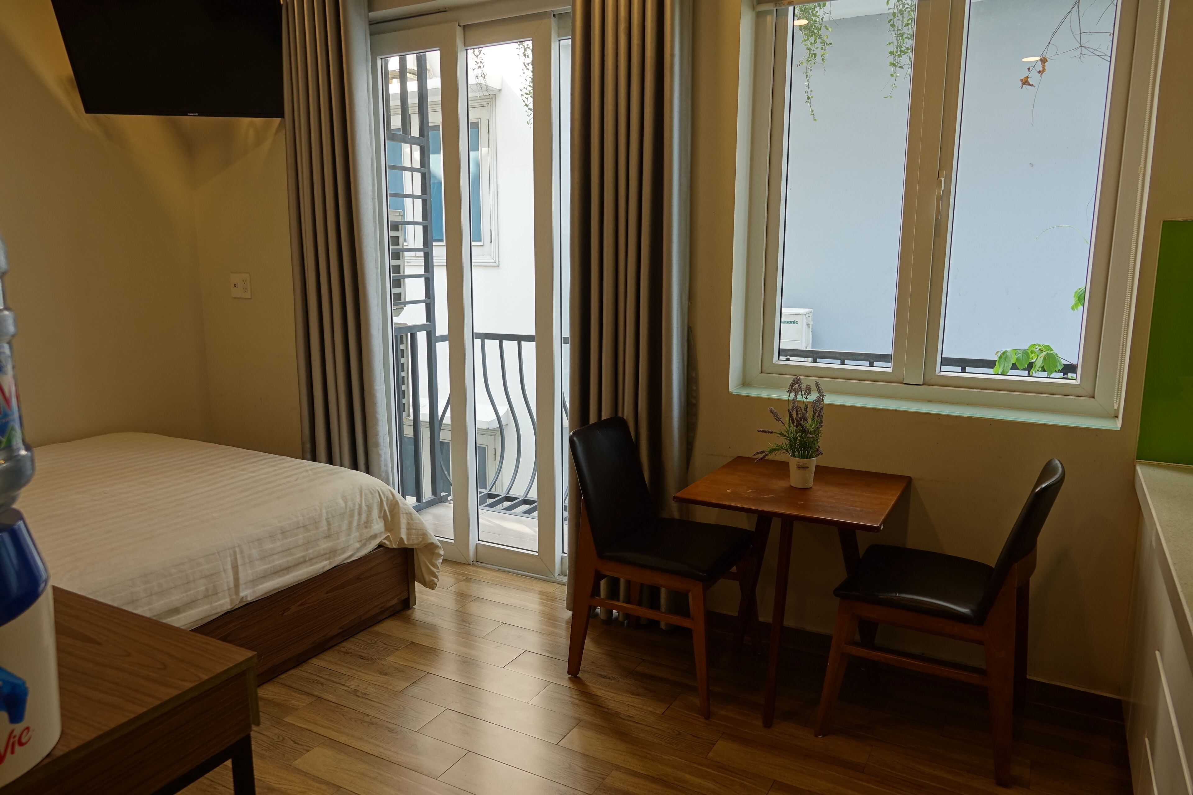 Een hotelkamer met een bed, een kleine tafel met stoelen, een raam met uitzicht en een balkon met gordijnen.