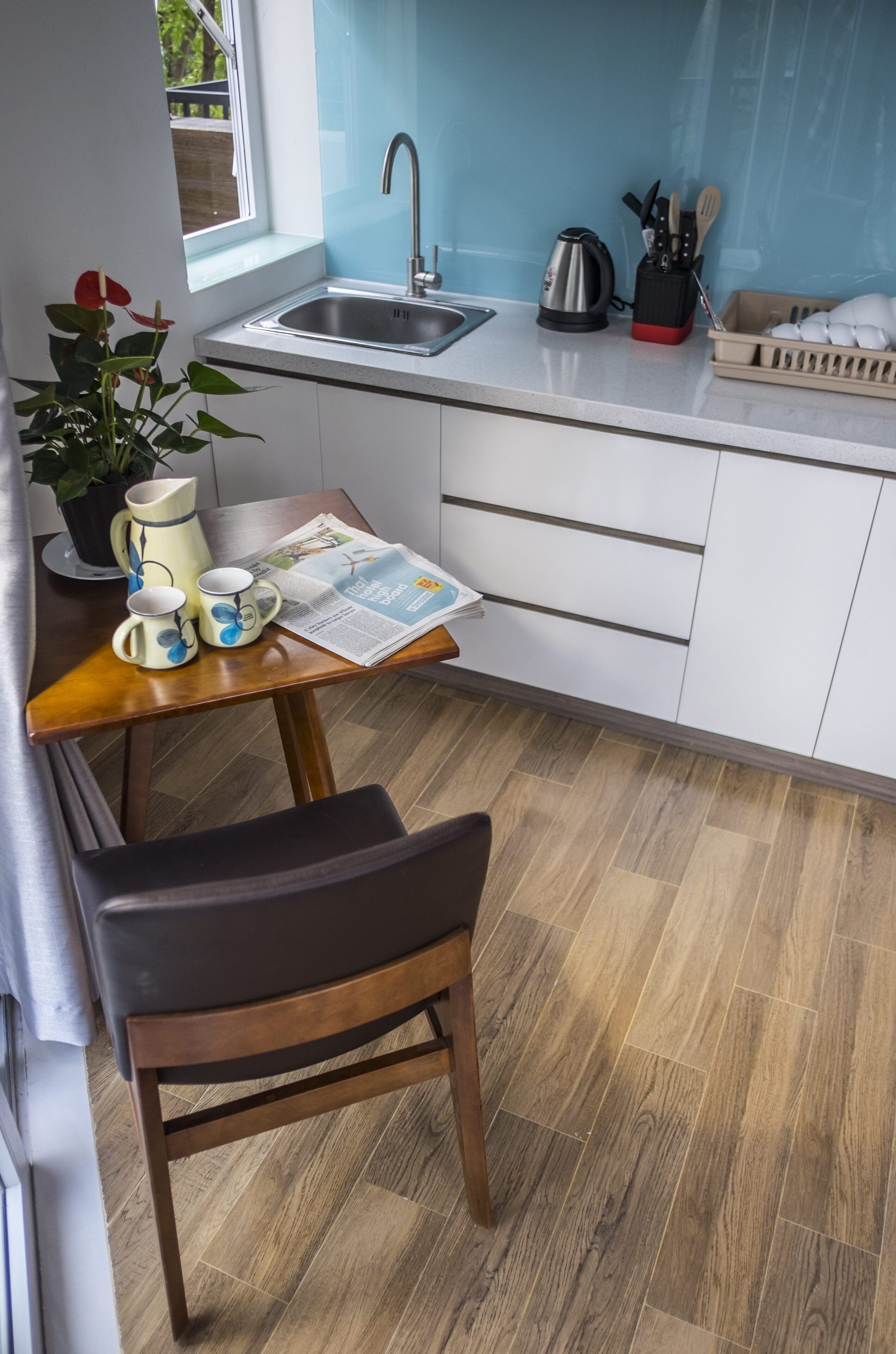 Una cucina moderna con lavello, bollitore e macchina per il caffè. C'è un tavolo con un giornale e una pianta in vaso.