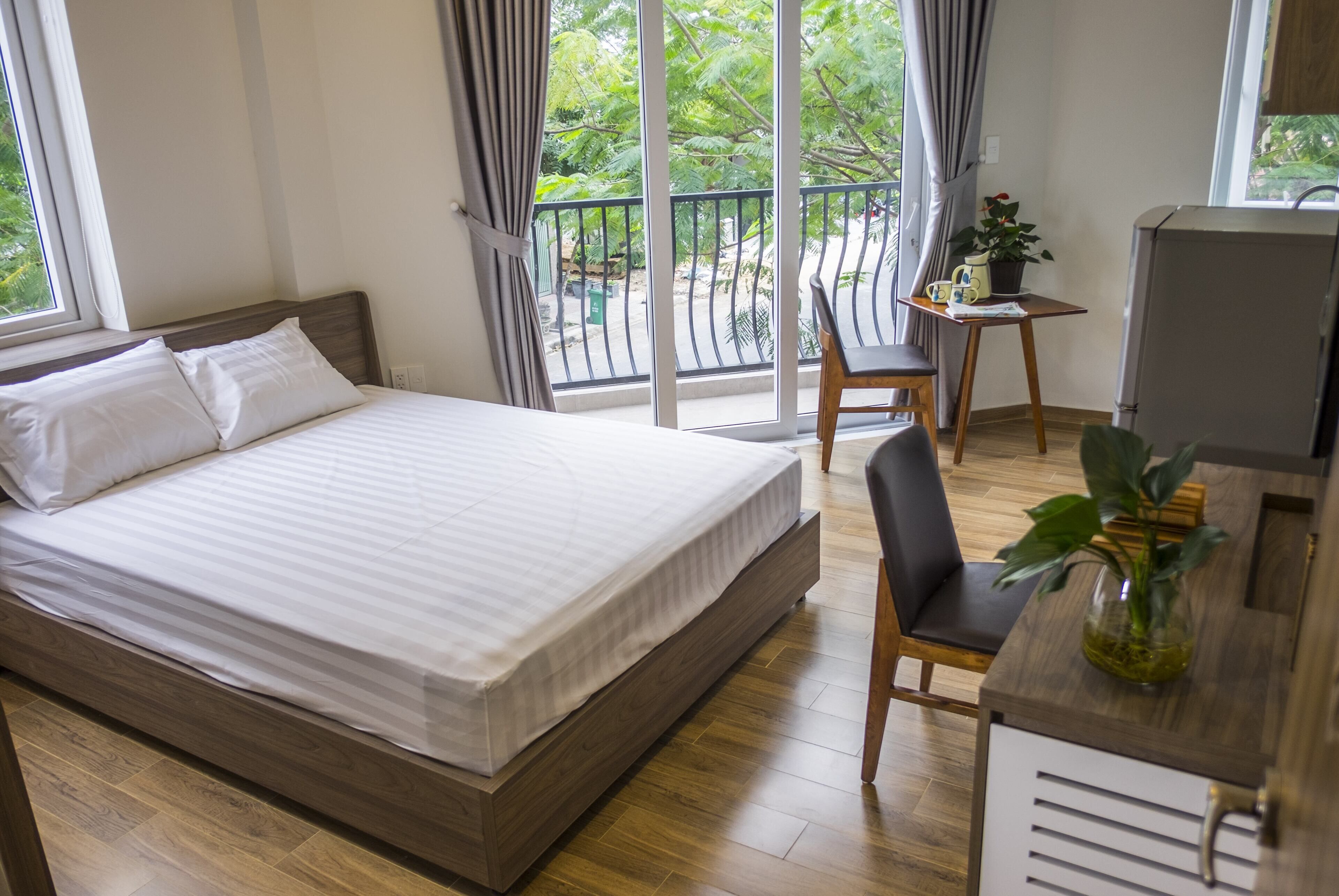 Une chambre d’hôtel comprenant un lit, un bureau avec une chaise, une télévision et un balcon donnant sur un espace verdoyant.