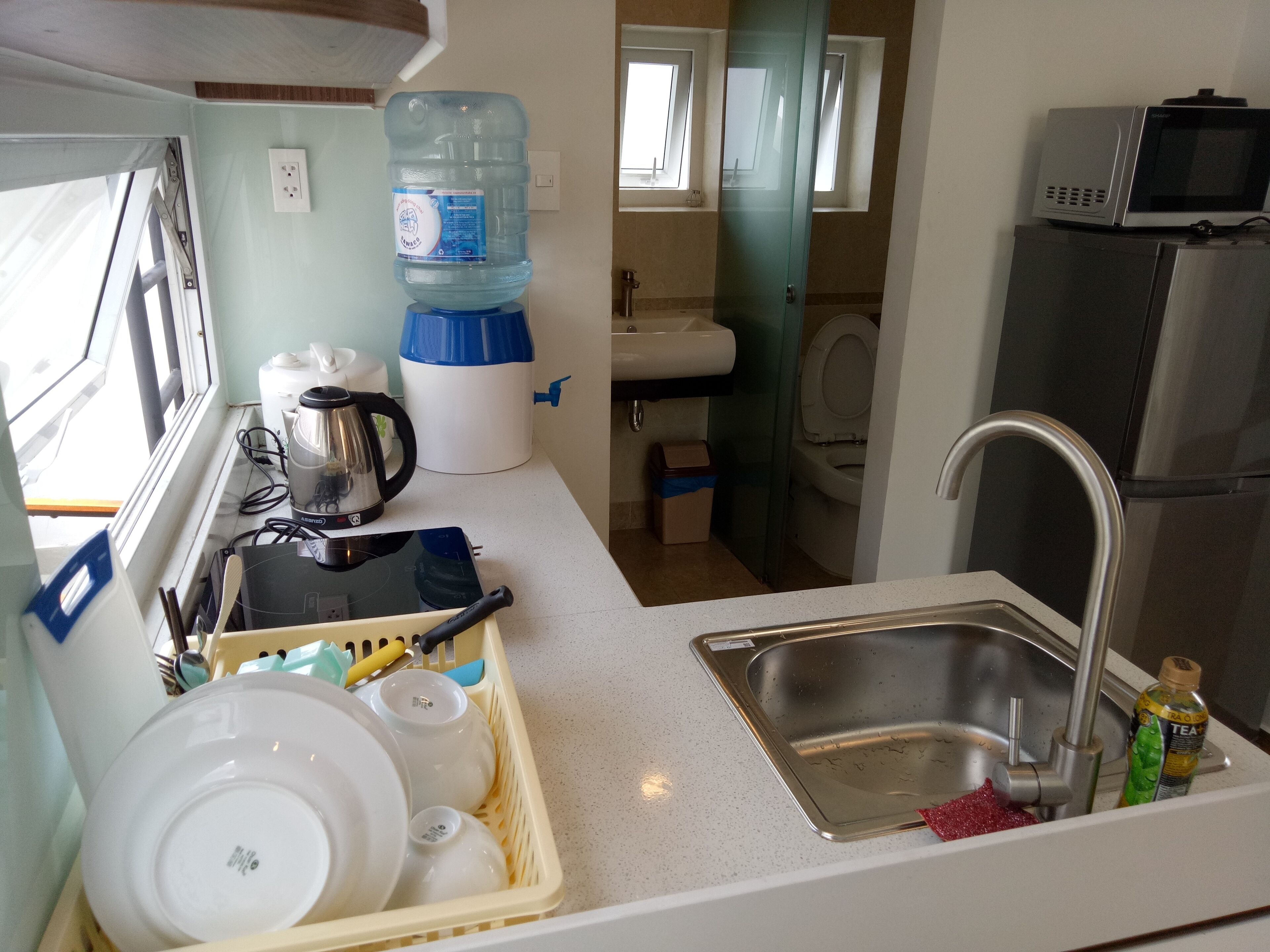 A compact kitchen with a sink, a kettle, a water dispenser, and a microwave.