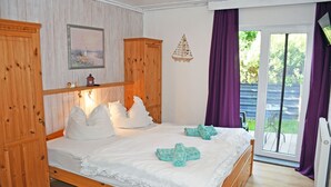 Un dormitorio con una cama de madera, ropa de cama blanca, un cuadro y vistas a través de un ventanal.