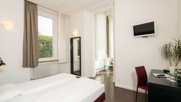 Una habitación de hotel con cama, escritorio, silla, televisor y ventana con cortinas.