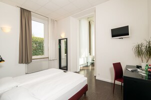 Una habitación de hotel con cama, escritorio, silla, televisor y ventana con cortinas.