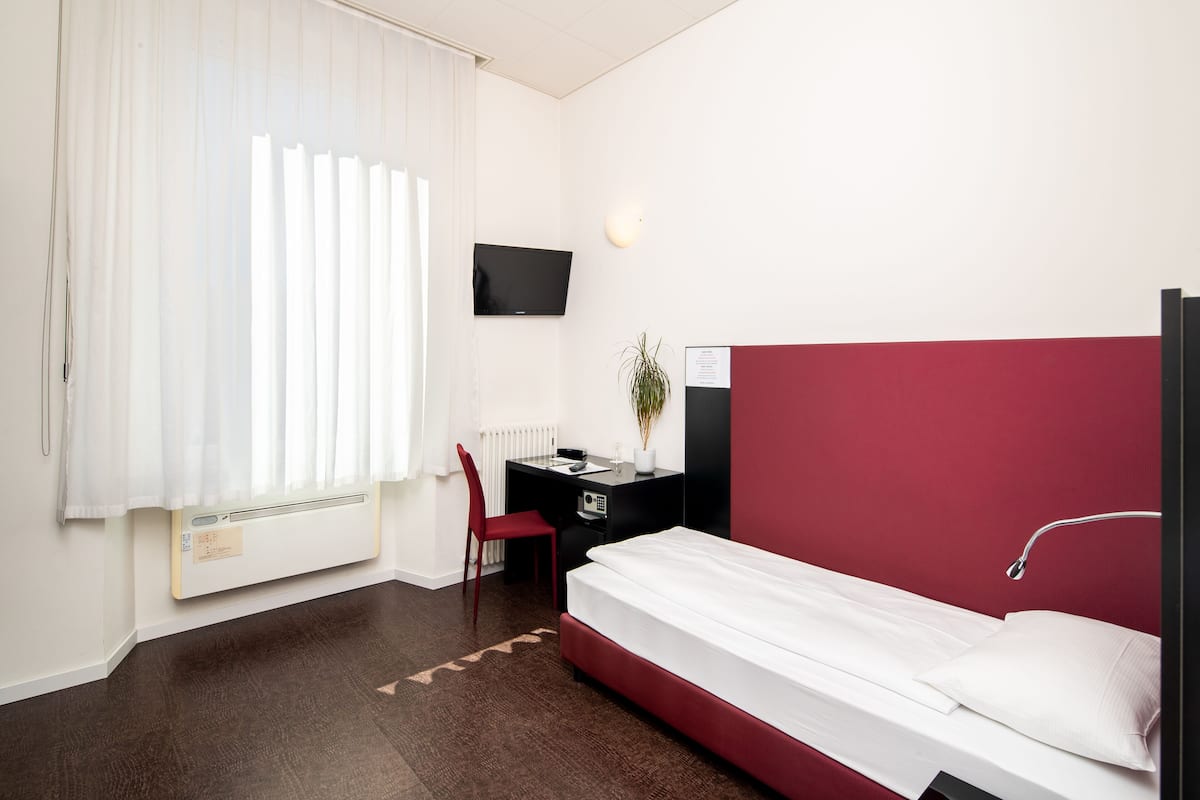 A hotel room with a bed, a desk, a chair, a TV, and a radiator.
