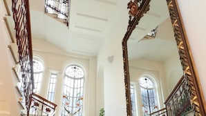 Una imponente escalera con un espejo grande y decorativo, y una planta en maceta en la parte superior.
