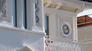 Un edificio con fachada blanca, molduras decorativas y un balcón con barandilla de metal ornamentada.