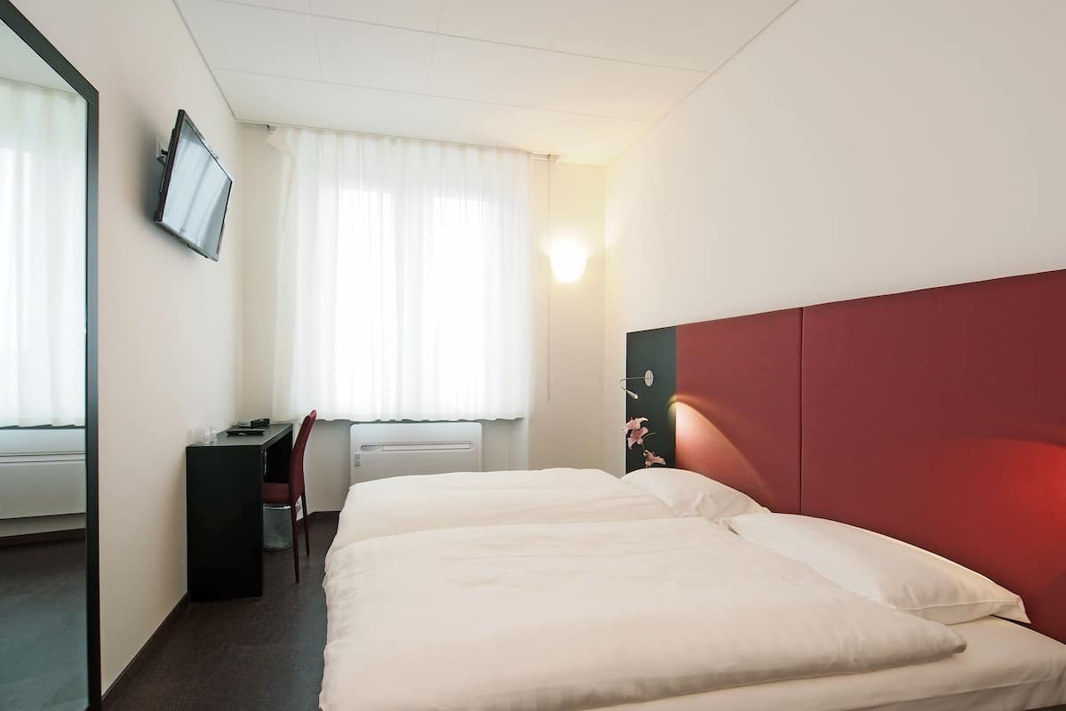 A hotel room with two beds, a desk, a chair, a TV, and a window with curtains.