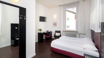 Una camera d'albergo con un letto, una scrivania, una sedia, una televisione e una finestra con tende.