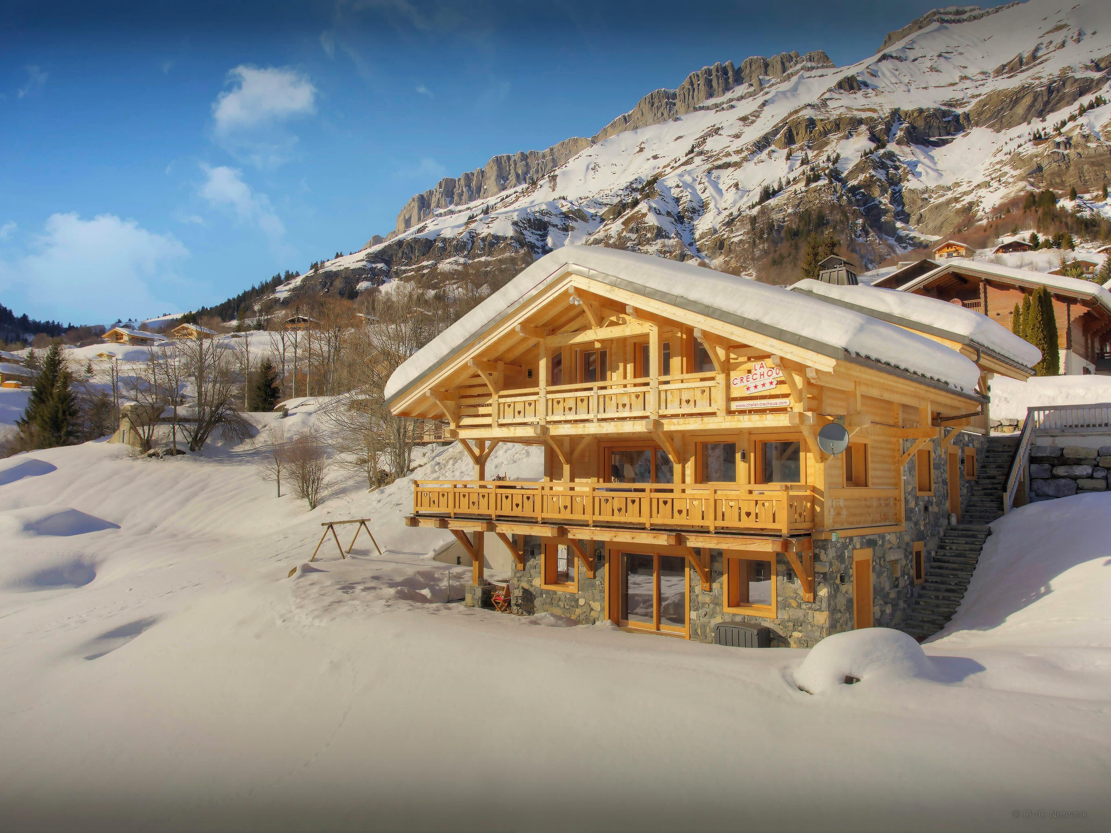 Een houten chalet met een balkon, gelegen in een besneewd bergachtig gebied.