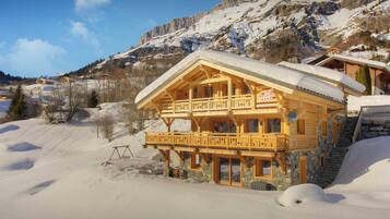 Een houten chalet met een balkon, gelegen in een besneewd bergachtig gebied.