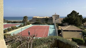 Ein Tennisplatz mit Blick auf das Meer und ein Gebäude im Hintergrund.