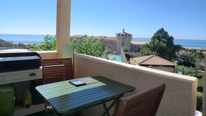 Ein Balkon mit Tisch und Stühlen, mit Blick auf eine Küstenlandschaft mit Gebäuden und einem klaren Himmel.