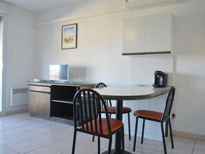 Una habitación pequeña y limpia con escritorio, dos sillas, cafetera y televisor.