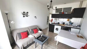 A compact living space with a sofa, a small table, a washing machine, and a kitchenette. - Oceanfront 2-Room Apt with Direct Beach Access in Les Sables-d'Olonne (Les Sables-d'Olonne)