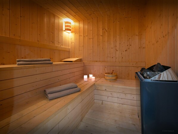 A wooden sauna with benches, a wall-mounted light, and a bucket of stones.