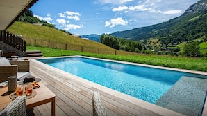 A pool area with a wooden deck, wicker furniture, and a view of a mountainous landscape. - Chalet Bonnevie - family home for 10, spa & mountain views - OVO Network (Les Villards-sur-Thônes)