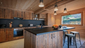 A modern kitchen with wooden cabinetry, a central island, and pendant lighting. - Chalet Bonnevie - family home for 10, spa & mountain views - OVO Network (Les Villards-sur-Thônes)