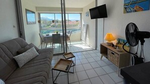 A living room with a sofa, a table, a TV, and a fan. - Beachfront Studio 4 Sleeps, Pool, Parking, near Argèles-sur-Mer Center (Argelès-sur-Mer)