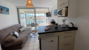 A compact living space with a kitchenette, a sofa, a dining table, and a view through a glass door. - Beachfront Studio 4 Sleeps, Pool, Parking, near Argèles-sur-Mer Center (Argelès-sur-Mer)