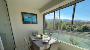 A dining area with a table set for two, a framed picture on the wall, and a view of mountains and greenery outside. - Beachfront Studio 4 Sleeps, Pool, Parking, near Argèles-sur-Mer Center (Argelès-sur-Mer)