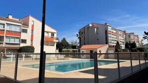 A swimming pool area with a clear sky, surrounded by multi-story buildings with balconies and a lamp post. - Beachfront Studio 4 Sleeps, Pool, Parking, near Argèles-sur-Mer Center (Argelès-sur-Mer)