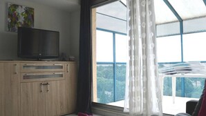 Ein Schlafzimmer mit großem Fenster, einem Fernseher auf einer Holzkassette und einem Balkon mit Aussicht.