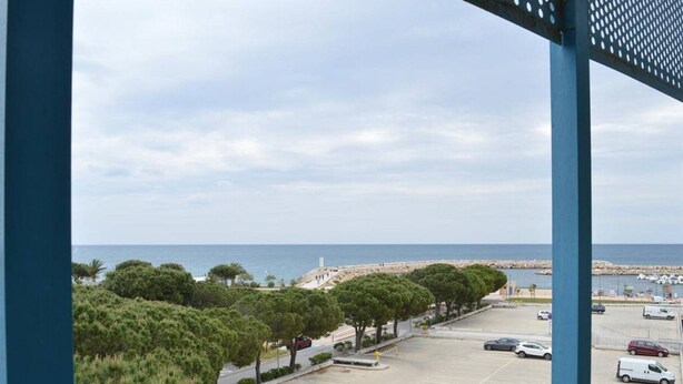 Ein Parkplatz mit Autos, Blick auf das Meer und Bäume.