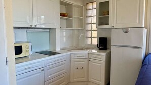 Eine kompakte Küche mit weißen Schränken, einer Mikrowelle, einer Kaffeemaschine und einem Kühlschrank.