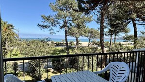 Ein Balkon mit Tisch und zwei Stühlen, mit Blick auf einen Strand und einen klaren Himmel.