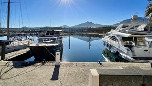 Un port de plaisance avec des bateaux amarrés, un ciel dégagé et une montagne en arrière-plan.