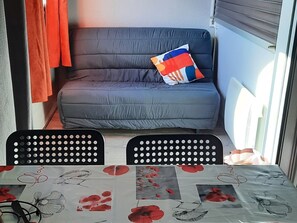 A room with a grey sofa, a colorful pillow, and a table with a floral tablecloth.