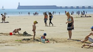 A beach with people, a lighthouse, and a bridge in the background.