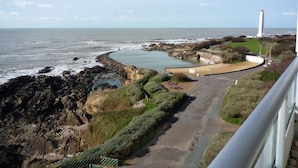 A coastal view with rocky terrain, a lighthouse, and a curved pathway leading to a beach.