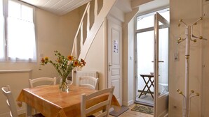 A dining area with a wooden table and white chairs, a vase with flowers, a staircase, and a coat rack.