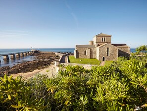 Una iglesia costera con fachada de piedra, un césped y un muelle que se adentra en el mar.