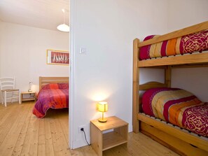 Un dormitorio con literas, una mesita de noche con lámpara, una silla y un cuadro en la pared.