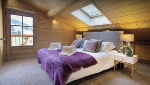 A cozy bedroom with a large bed, a skylight, a wooden door, and a nightstand with a lamp. - Chalet Le Mousqueton - ski base for 14 spa & mountain views - OVO Network (La Clusaz)
